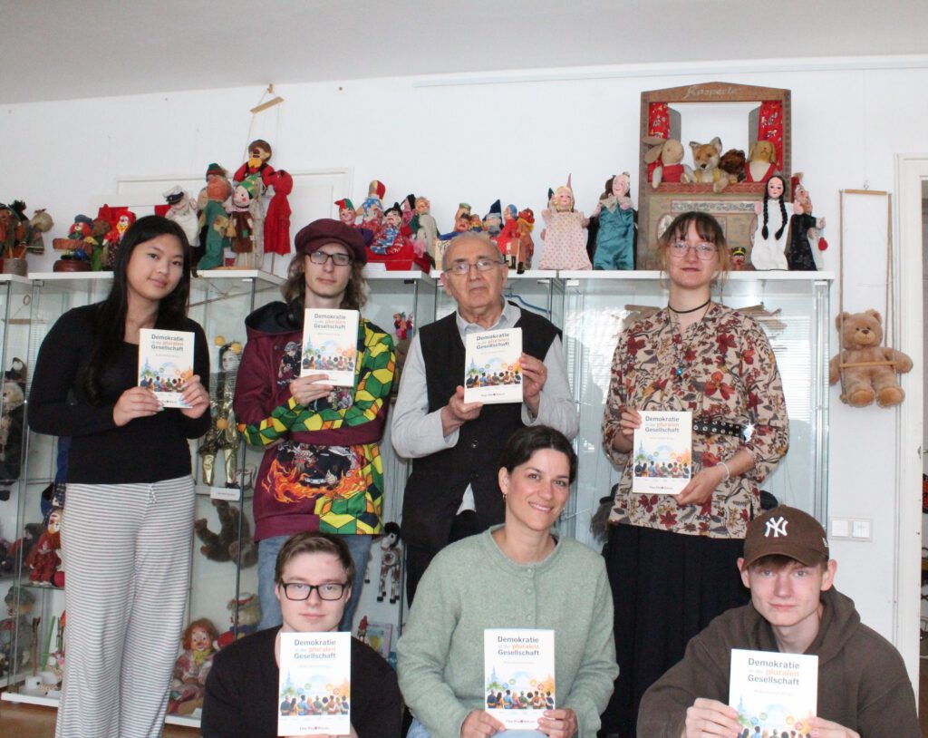 Molla Demirel mit Jugendgruppe hält das neu erschienene Buch „Demokratie in der pluralen Gesellschaft“ (Foto: Radio Kaktus Münster e.V. / Greta Börding)